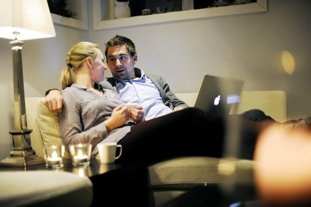 Et par ligger i sofaen med datamaskinen på fanger og planlegger boligkjøp.