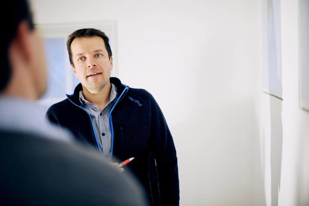 Mann står mot kamera og lytter til annen mann vendt vekk fra kameraet. 